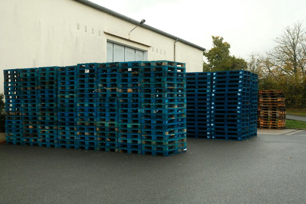 Stack of blue plastic pallets outside an industrial building.