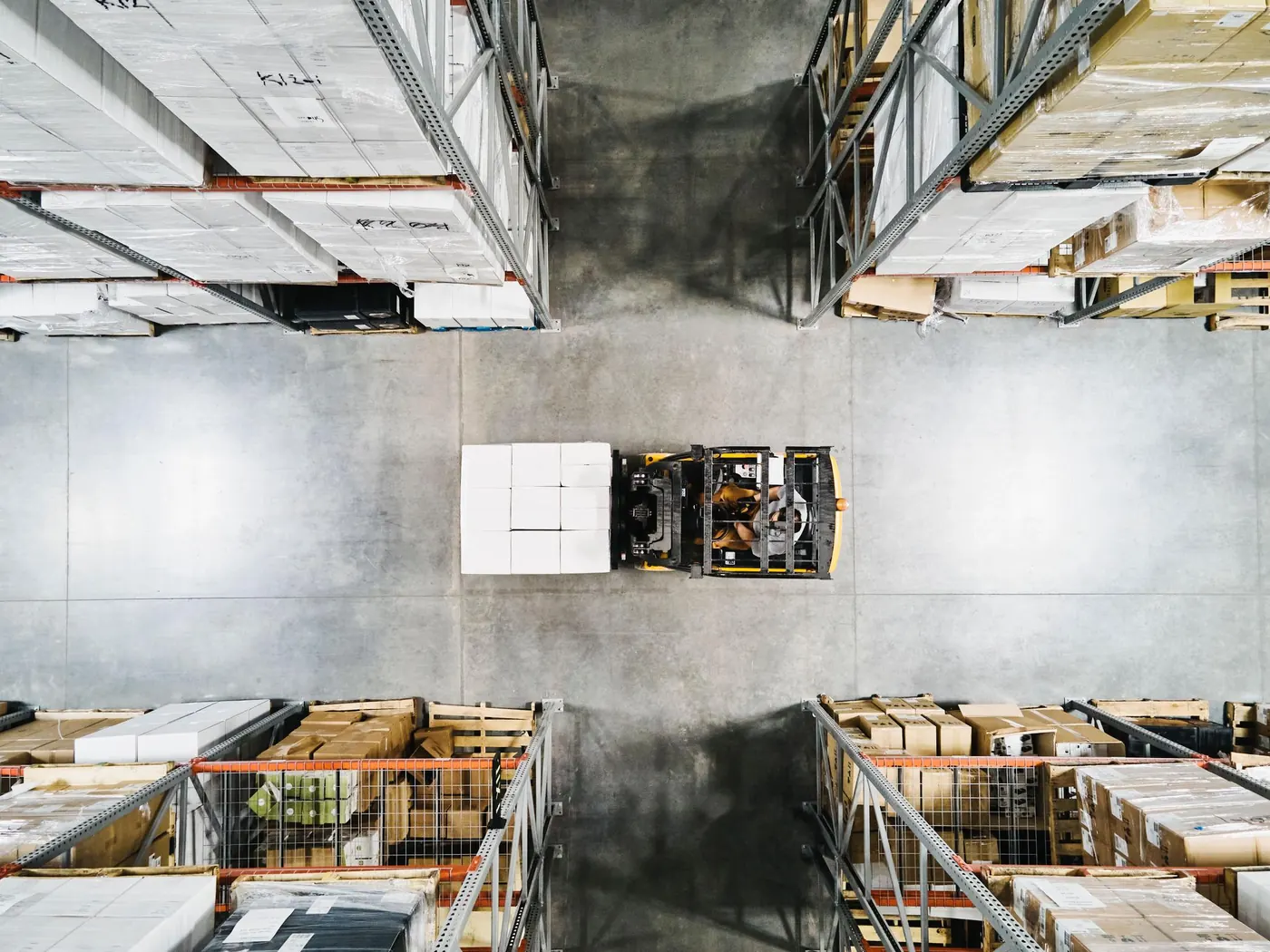 Overhead view of a forklift moving a wrapped pallet load between warehouse racks, ready for immediate shipment.
