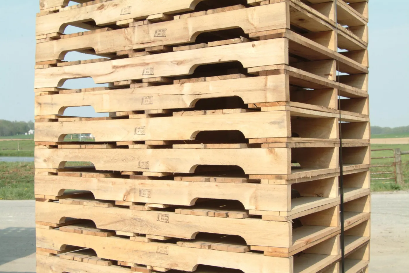 Stack of new wooden pallets outdoors with a farm landscape in the background.